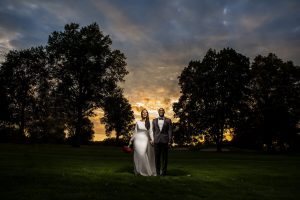 wedding couples poses outdoors in front of trees and sunset