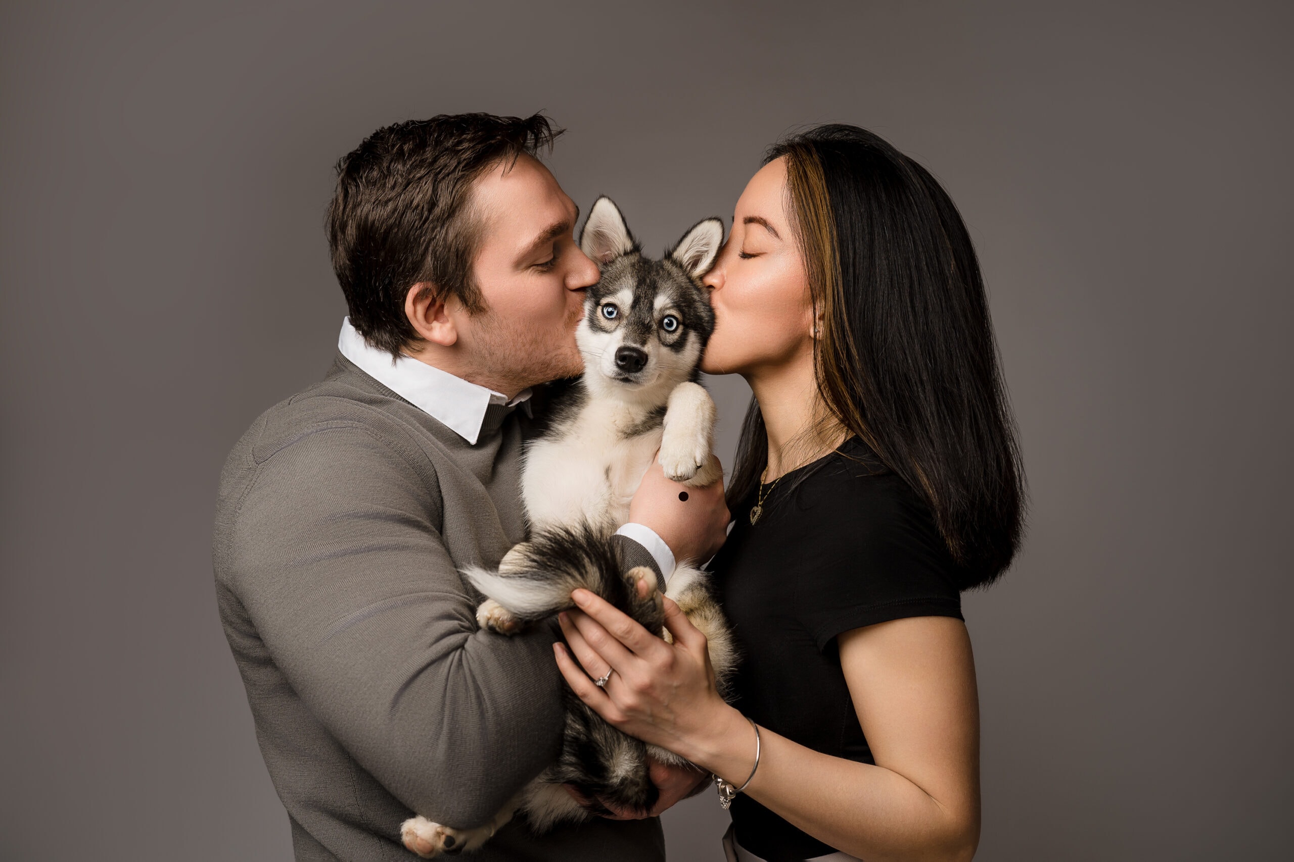 Parents kiss they Husky puppy while he bends his paw down for an adorable picture.