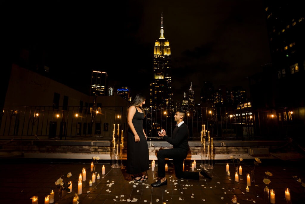 Man proposing on a candlelit NYC rooftop with the Empire State Building lit up in the background